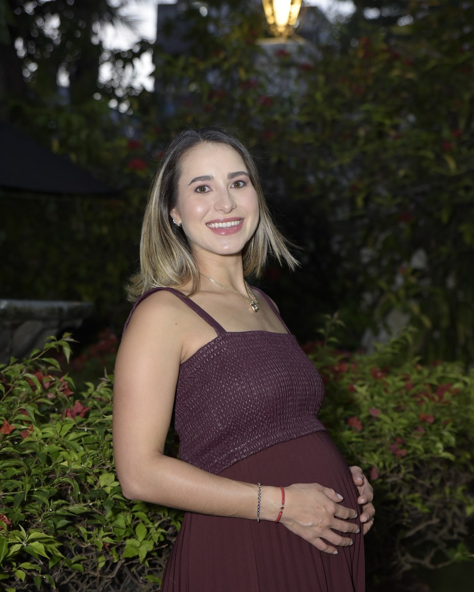 Mafe smiling in a burgundy dress, hand on her baby bump